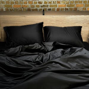 Puede incluir: Una cama negra con una cabecera de madera y ropa de cama negra. La cama está contra una pared de ladrillo.