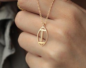 Könnte beinhalten: Eine goldfarbene Anhänger-Halskette mit einem Football-Design. Der Anhänger hat eine ovale Form mit detaillierten Linien und einer Kette. Die Halskette ist ein zartes Schmuckstück.