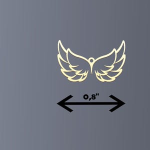 Puede incluir: Un par de alas doradas estilizadas con un peque&ntilde;o detalle circular en el centro superior. La envergadura mide 2 cm. Las alas est&aacute;n sobre un fondo gris.