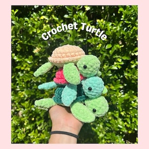 Peut inclure: Plusieurs tortues crochetées colorées, dans des tons de vert, rose et pêche. Le texte "Crochet Turtle" est écrit dans une police manuscrite. Les tortues sont faites à la main et semblent douces et moelleuses.
