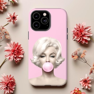 May include: A pink phone case featuring a portrait of Marilyn Monroe blowing a bubblegum bubble. The image has a light pink background. The phone case has a black camera module.