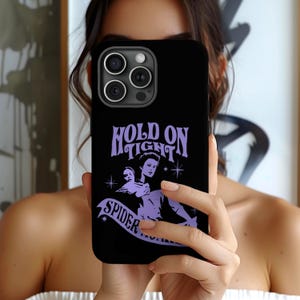 May include: Black phone case featuring a purple graphic with the text "Hold On Tight Spider Motherfucker". The design includes a vintage illustration of two figures. The phone case has a glossy finish.