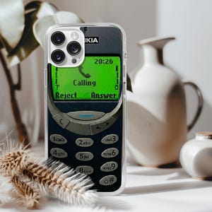 May include: A white ceramic mug with a black handle and the text "But First, Coffee" in a bold, black font. The mug is set against a blurred background, suggesting a cozy setting.