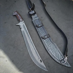 May include: A large, serrated blade knife with a dark wooden handle and a black leather sheath. The blade is gray with a saw-like edge and a curved tip. The sheath has a textured pattern and a shoulder strap.
