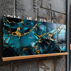 Può includere: Orologio da parete rettangolare con un design in marmo verde acqua e oro. Il quadrante dell'orologio presenta numeri romani e lancette dorate. L'orologio è montato su una mensola di legno contro un muro grigio strutturato.