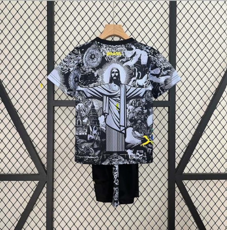 Puede incluir: Conjunto de camiseta y pantal&oacute;n corto con gr&aacute;ficos en blanco y negro con una ilustraci&oacute;n detallada de Cristo Redentor con los brazos extendidos. La camiseta tiene cuello redondo y mangas cortas. El pantal&oacute;n corto es negro. La palabra "BRASIL" es visible en la camiseta.
