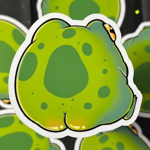 Könnte beinhalten: Eine Sammlung von Cartoon-Frosch-Aufklebern. Jeder Aufkleber zeigt einen grünen Frosch mit dunkelgrünen Flecken und einem weißen Umriss. Der Frosch ist von hinten dargestellt, mit gelben Akzenten. Die Aufkleber sind auf einem dunklen Hintergrund angeordnet.