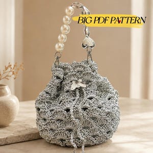 May include: A silver crochet drawstring bucket bag featuring a scalloped pattern, a butterfly charm, and a handle made of white faux pearls and silver heart-shaped beads. The image includes the text BIG PDF PATTERN in a yellow highlight.