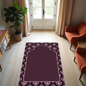 May include: A burgundy prayer rug with a decorative arch design. The rug has a dark background with a repeating floral pattern in pink and black. The central area is a solid burgundy color, framed by a pink border.
