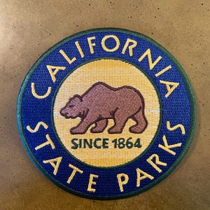 May include: A blue and yellow round patch with the text "California State Parks" and a brown bear silhouette. The text "Since 1864" is inside the circle.