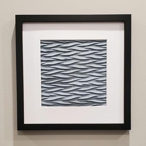 May include: Framed artwork featuring a textured, wave-like pattern in shades of gray and white. The artwork is set within a white mat and a black frame, creating a modern and minimalist aesthetic. The piece is suitable for home or office decor.