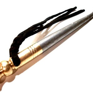 May include: A silver and gold metal tool with a black leather cord. The tool has a pointed tip and a rounded handle.
