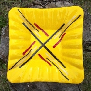 May include: A yellow square glass dish with a black, white, and red geometric design.