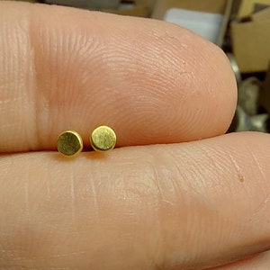 Puede incluir: Dos peque&ntilde;os pendientes redondos de color dorado.
