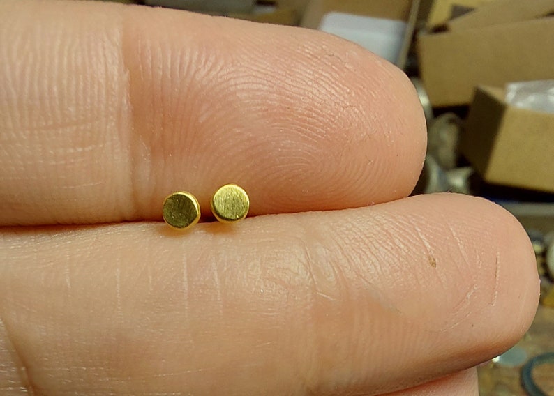 Puede incluir: Dos peque&ntilde;os pendientes redondos de color dorado.