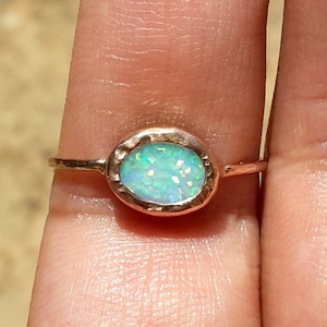 May include: A delicate gold ring with a light green opal gemstone set in a hammered oval bezel.