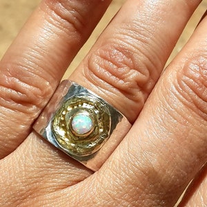 May include: A silver and gold ring with a white opal gemstone set in a textured band.