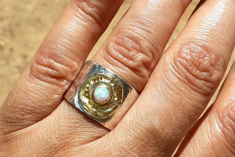 May include: A silver and gold ring with a white opal gemstone set in a textured band.