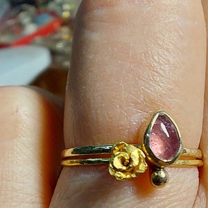 May include: A gold ring with a pink gemstone and a gold flower design.