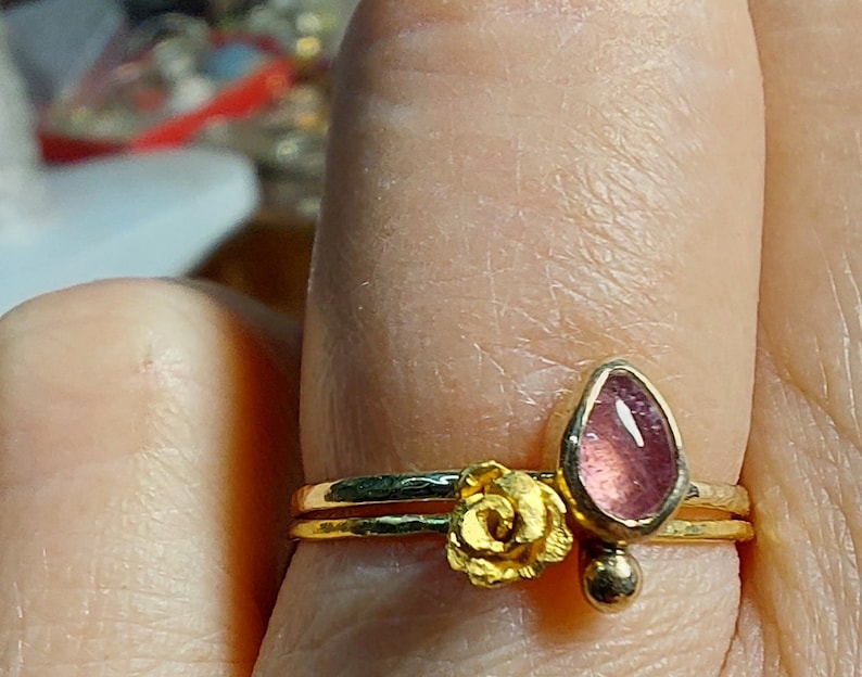 May include: A gold ring with a pink gemstone and a gold flower design.