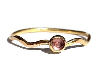 May include: A delicate gold ring with a wavy band and a single pink gemstone.