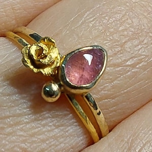 May include: A gold ring with a pink gemstone and a gold rose design.