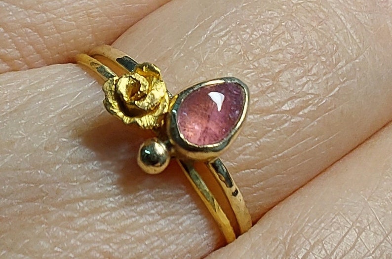 May include: A gold ring with a pink gemstone and a gold rose design.