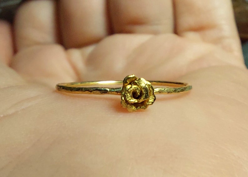 May include: A delicate gold ring with a textured band and a small rose-shaped design.