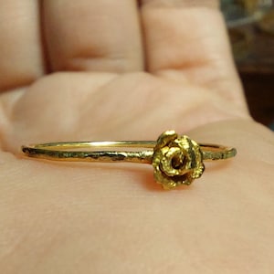May include: A gold ring with a rose design. The ring is simple and delicate, with a hammered texture.