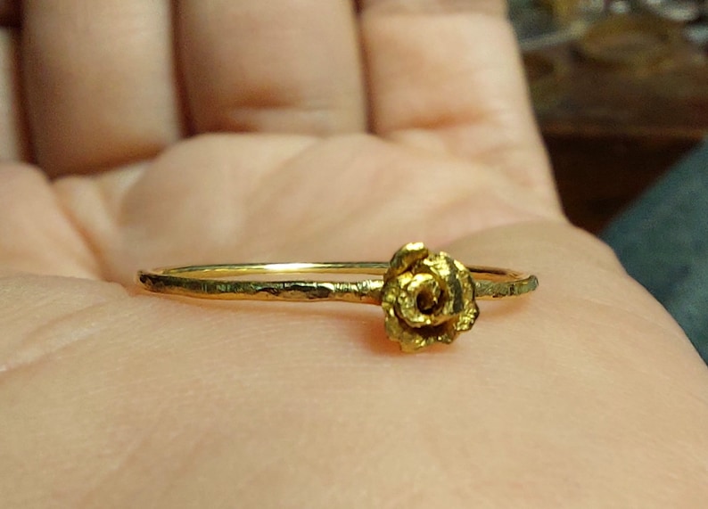 May include: A gold ring with a rose design. The ring is simple and delicate, with a hammered texture.