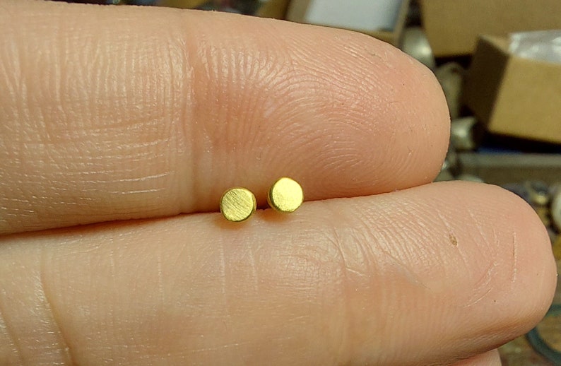 Puede incluir: Un par de peque&ntilde;os pendientes redondos de color dorado.