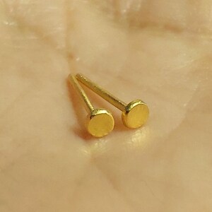 Puede incluir: Dos pendientes de bot&oacute;n dorados con tapas redondas.