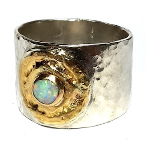 May include: A silver and gold ring with a hammered texture. The ring has a large opal gemstone set in a gold circle.