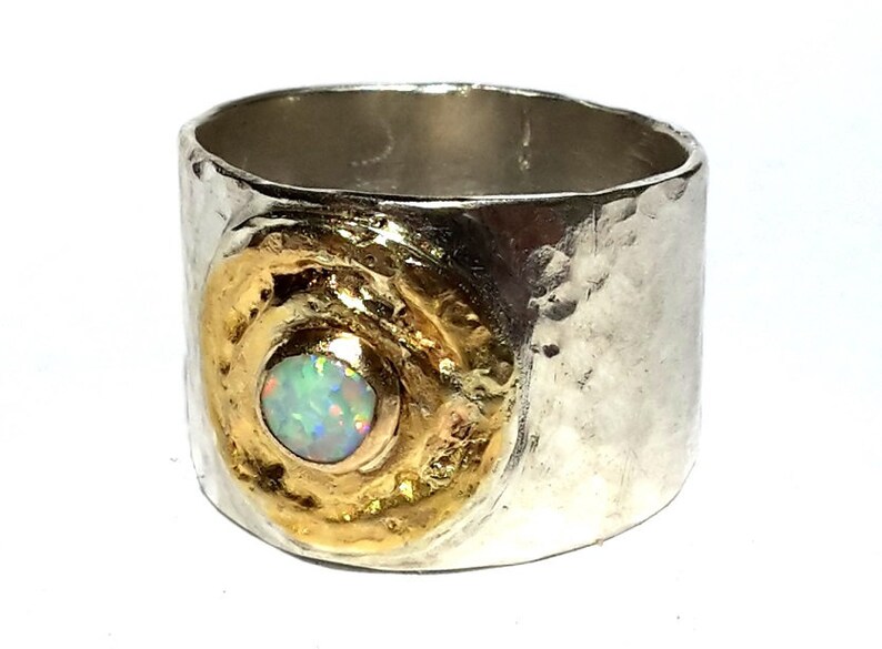 May include: A silver and gold ring with a hammered texture. The ring has a large opal gemstone set in a gold circle.