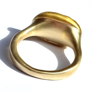 May include: A gold ring with a smooth, rounded band and a flat, oval-shaped top. The ring is made of a single piece of metal and has a polished finish.