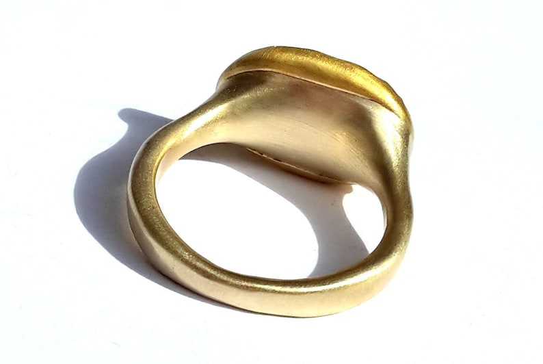 May include: A gold ring with a smooth, rounded band and a flat, oval-shaped top. The ring is made of a single piece of metal and has a polished finish.