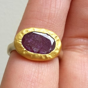 May include: A gold ring featuring a large, oval-shaped, purple gemstone set in a textured gold bezel.