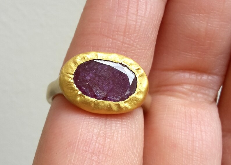 May include: A gold ring featuring a large, oval-shaped, purple gemstone set in a textured gold bezel.