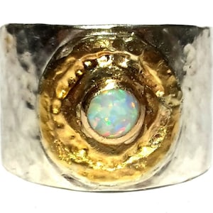 May include: A silver and gold ring with a large opal gemstone set in a textured gold circle. The ring is wide and has a hammered finish.