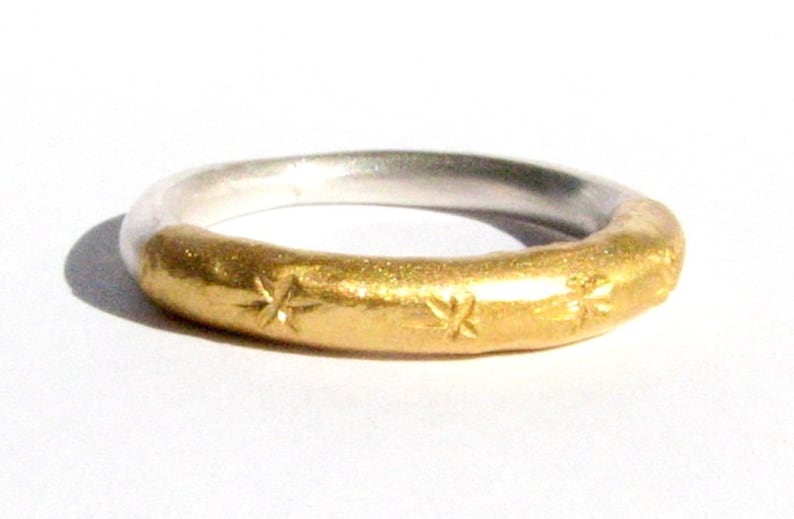 May include: A silver and gold ring with a textured band and star-shaped designs.