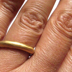 May include: A simple gold band ring worn on a finger.