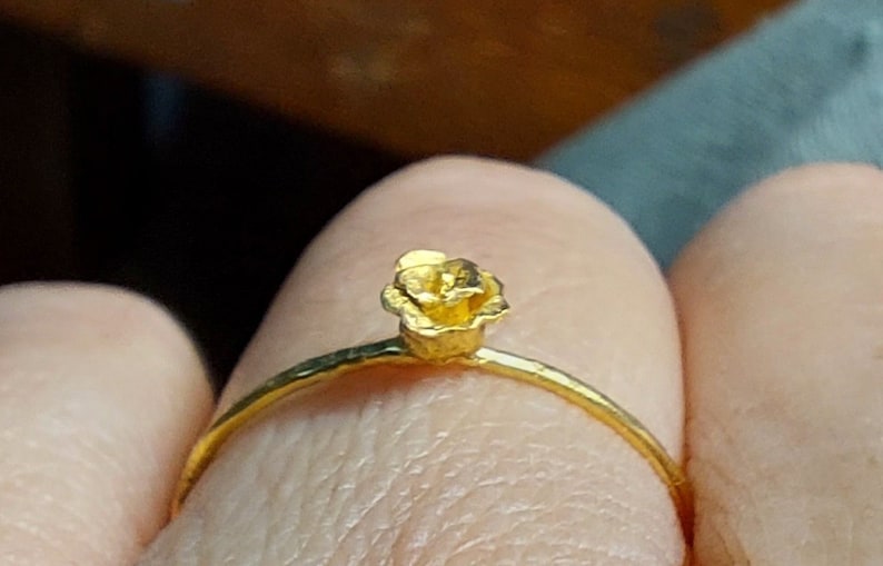 May include: A gold ring with a small, textured flower design.
