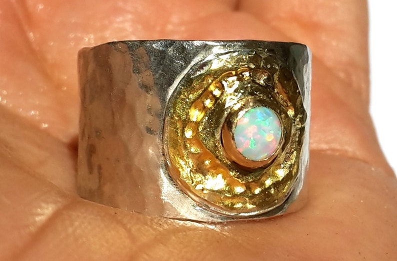 May include: A silver ring with a hammered texture and a gold-toned bezel set with a white opal gemstone.