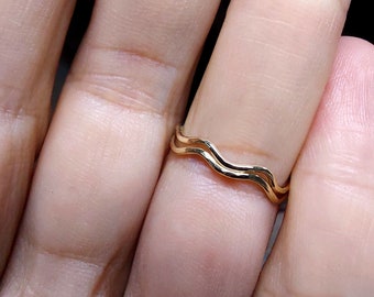 May include: A gold-toned ring with a wavy design. The ring is worn on a finger.