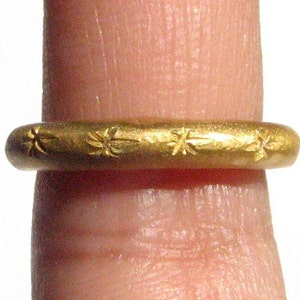 May include: A gold ring with a simple design featuring a repeating pattern of small stars.
