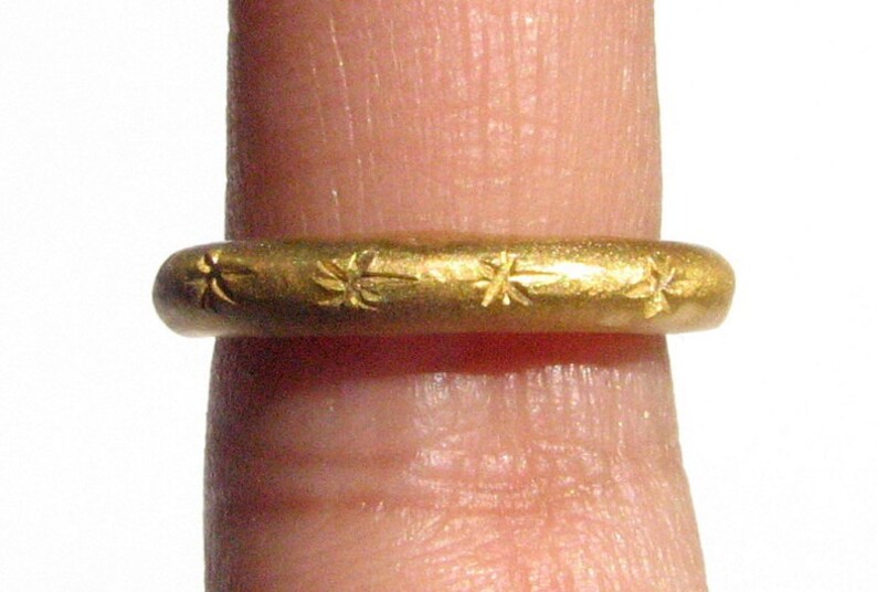 May include: A gold ring with a simple design featuring a repeating pattern of small stars.