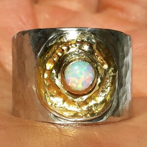 May include: A silver and gold ring with a hammered finish. The ring features a round opal gemstone set in a gold bezel.