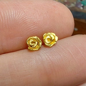 May include: A pair of gold rose-shaped stud earrings. The earrings are small and delicate, with a textured surface.