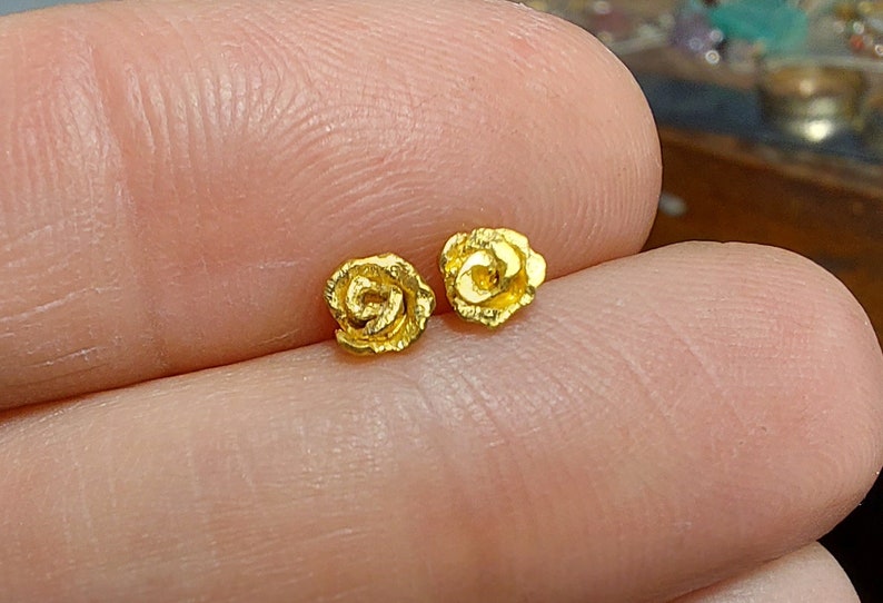 May include: A pair of gold rose-shaped stud earrings. The earrings are small and delicate, with a textured surface.