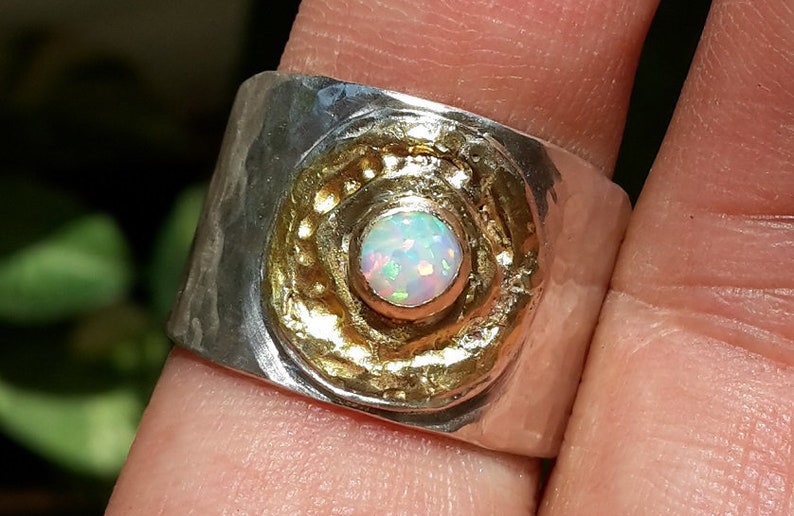 May include: A silver ring with a hammered texture and a gold circle with a white opal gemstone in the center.